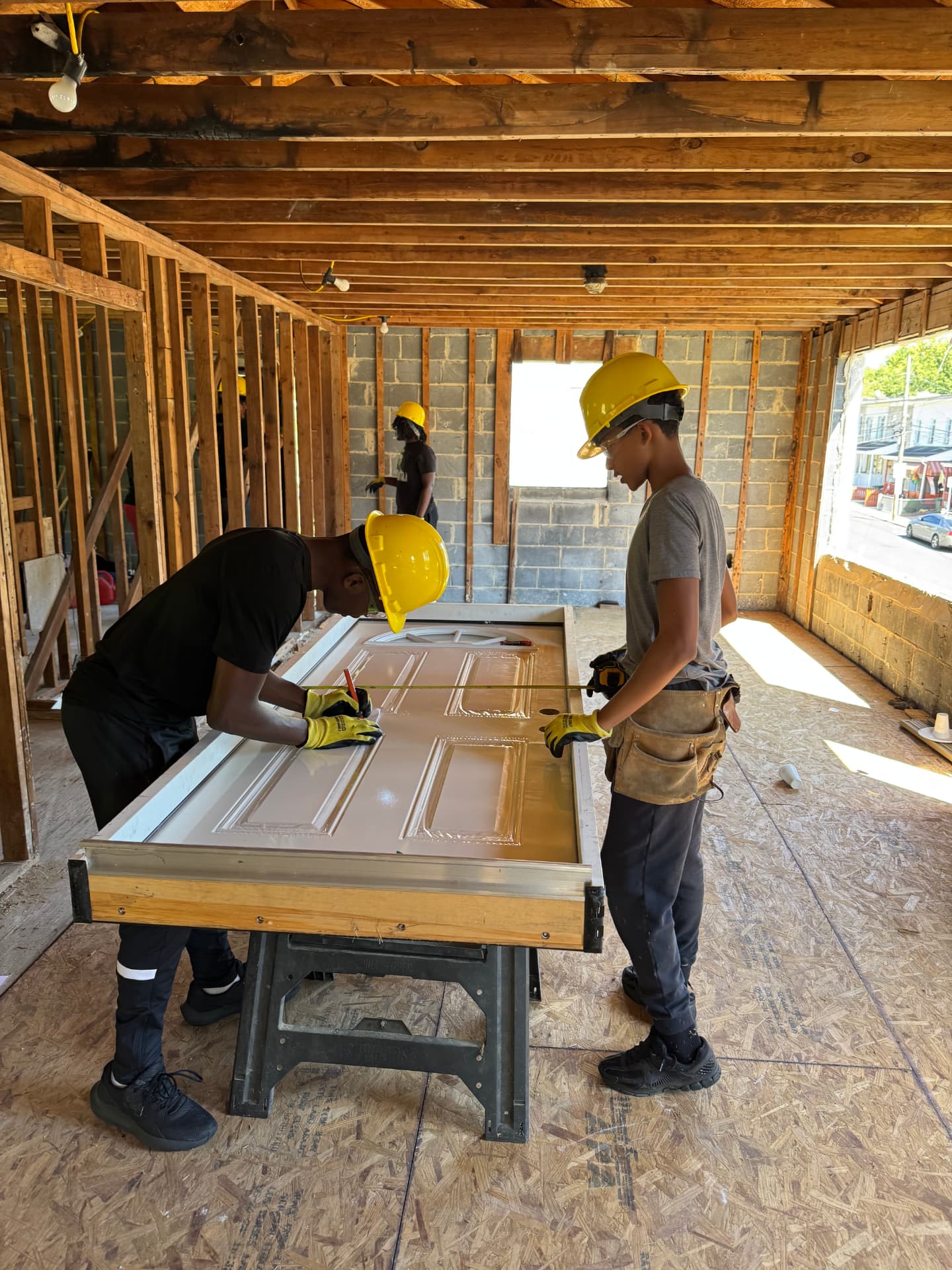 Two participants in hard hats measuring and marking a door on a jobsite